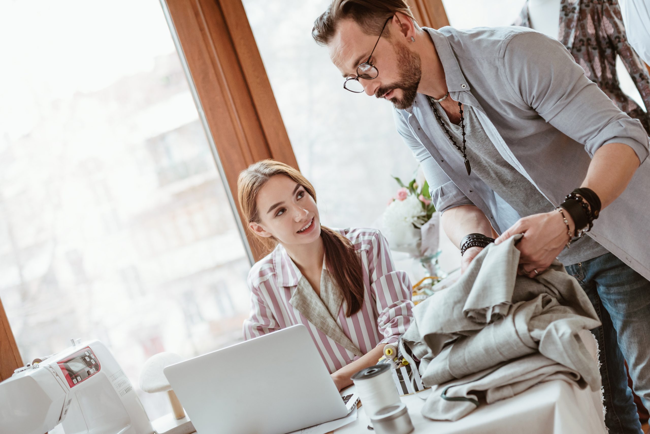 Two apparel designers reviewing fabric and product details together at a laptop