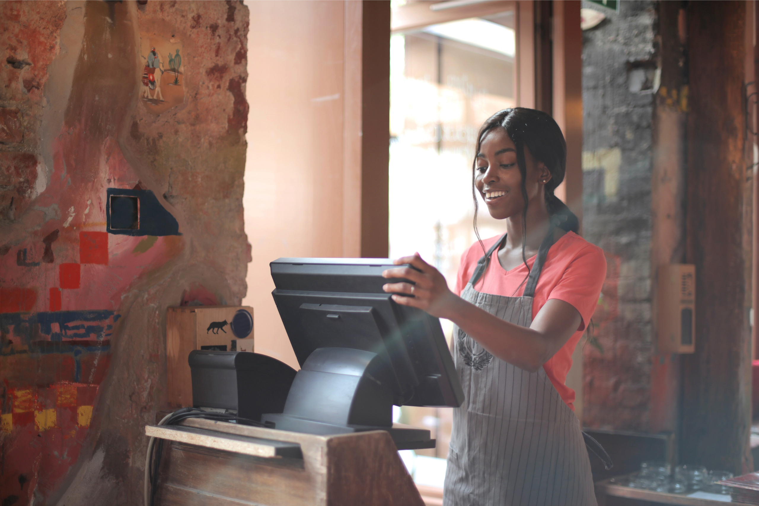 A smiling employee in an apron adjusting a point-of-sale terminal at a shop checkout counter