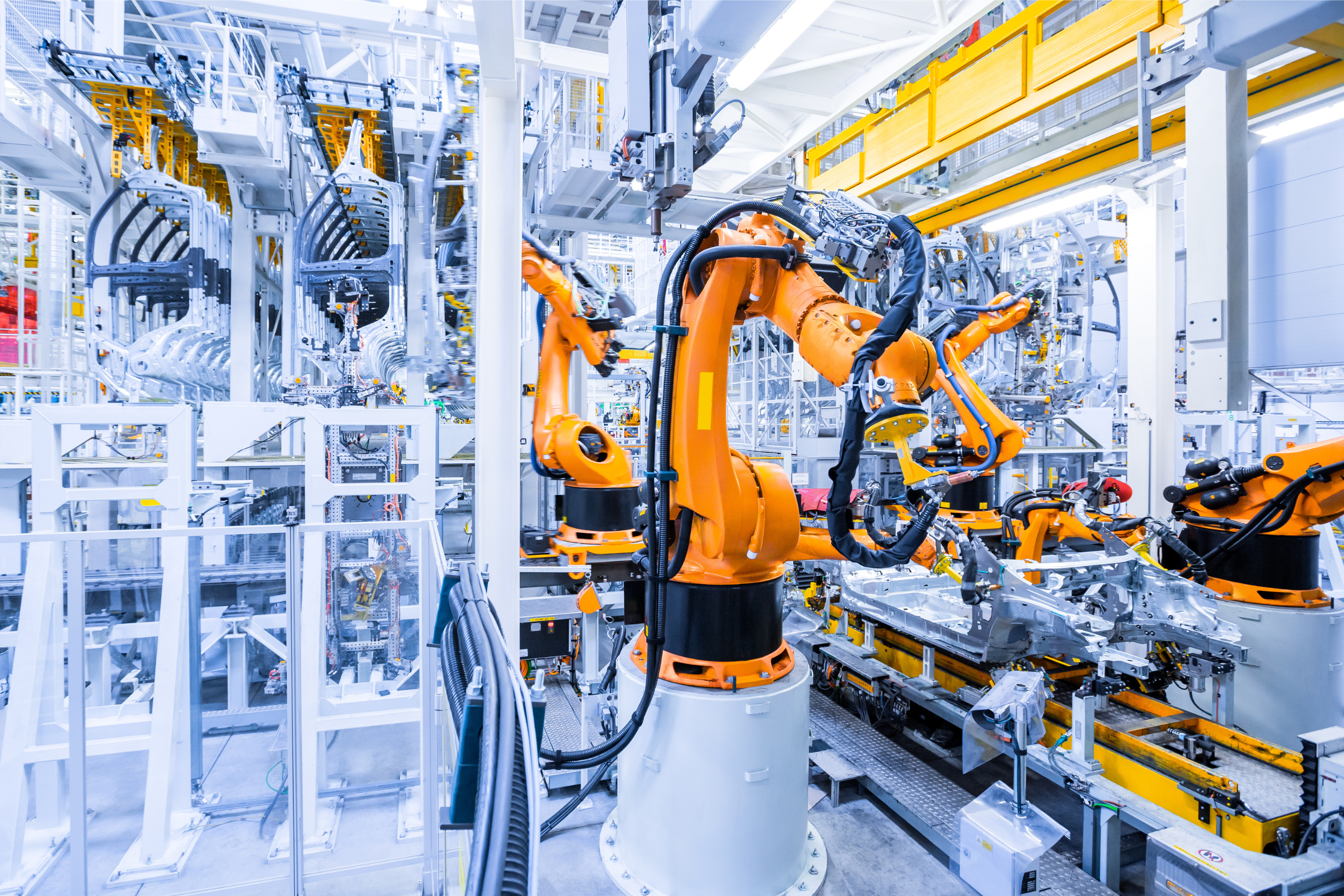 Orange robotic arms performing automated welding on car body frames along an automotive assembly line, representing automation in Novobi's Odoo manufacturing update