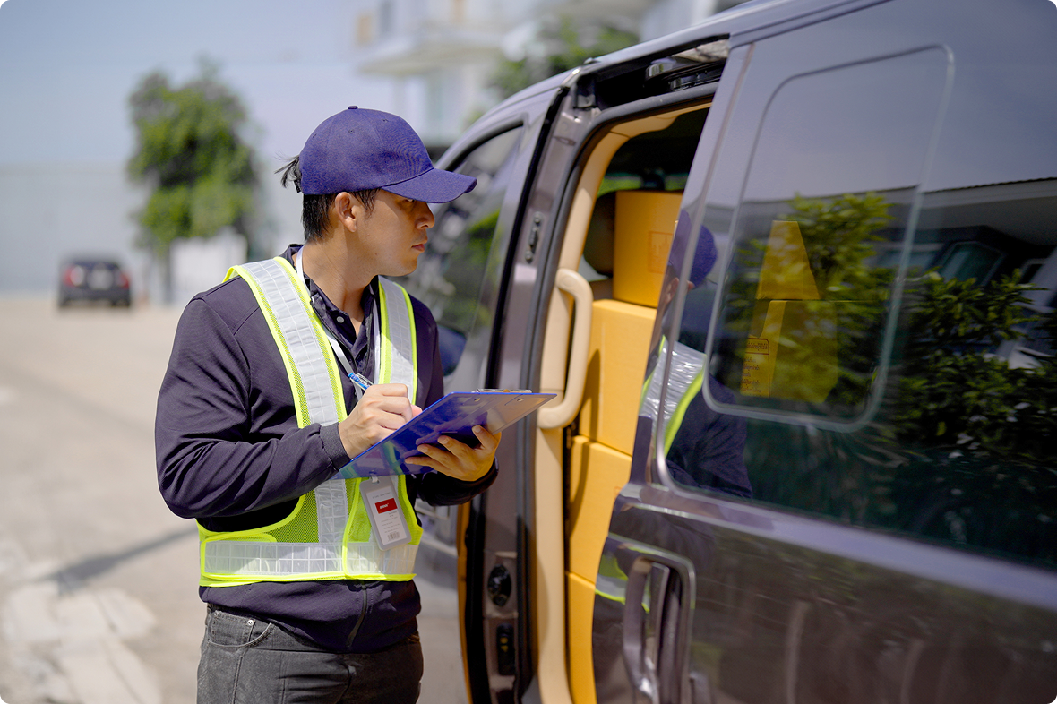 A field service technician in a safety vest checking a clipboard beside an open van loaded with boxes of parts